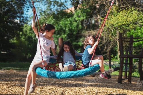 Preview: Portrait of three beautiful caucasian girls sisters ride together on a round rope swing in the park