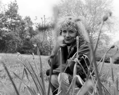 Preview: Monochrome portrait of curly woman looking at camera through plants in a park.