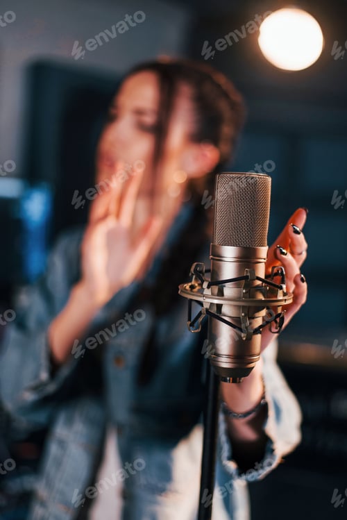 Preview: Close up view of microphone. Young beautiful female performer rehearsing in a recording studio