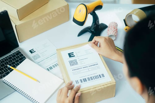 Preview: Young business owner putting shipping label on parcel.