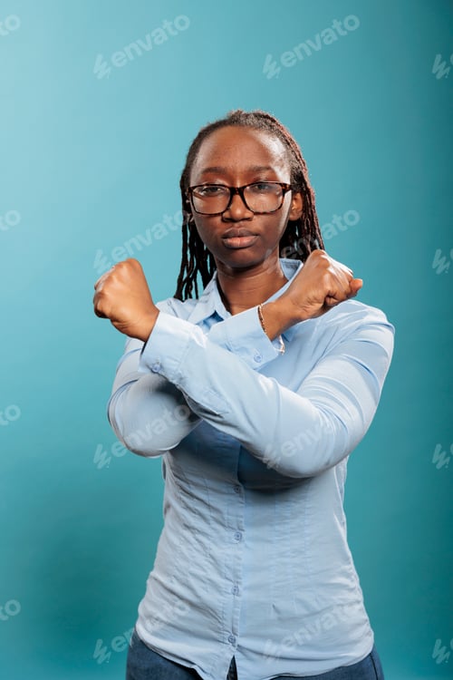 Preview: Confident and expressive woman making decline crossed arms symbol while standing on blue background.