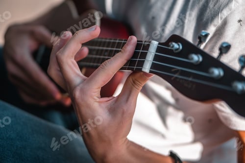 Preview: Shallow focus shot of a person wearing a white t-shirt while playing a song on the ukulele