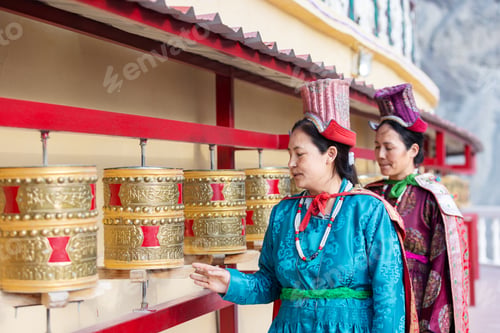 Preview: Two Indian women in traditional Leh attire spin golden prayer wheels at a monastery