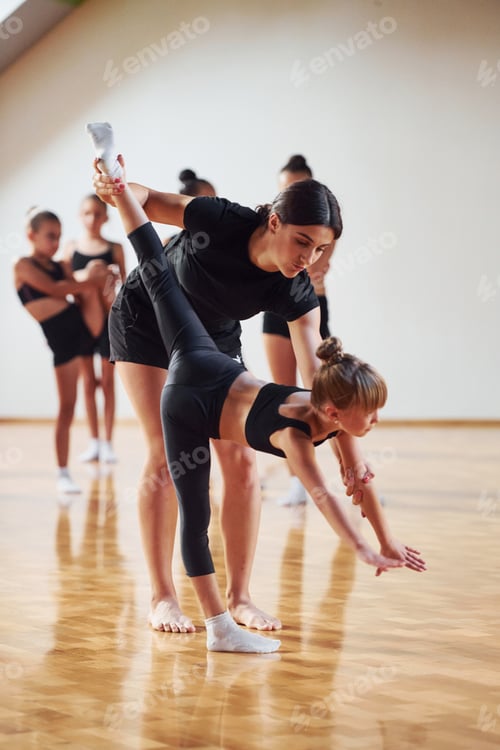 Preview: With help from coach. Group of female kids practicing athletic exercises together indoors