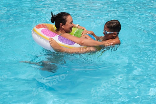 Preview: A boy with goggles clings to a float; his mother s support evident. This scene underscores the