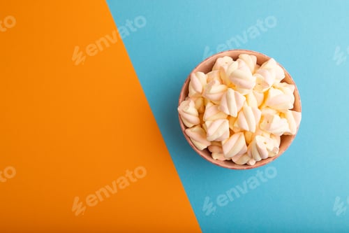Preview: Orange and pink marshmallow in ceramic bowl on blue and orange pastel paper, top view, copy space