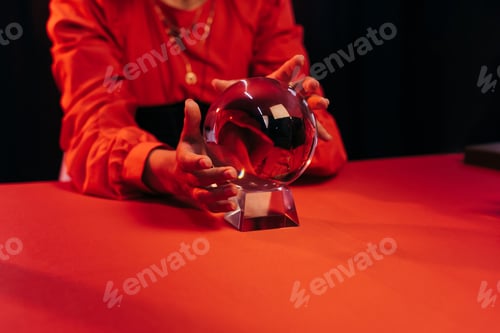Preview: partial view of fortune teller near crystal ball on red table isolated on black