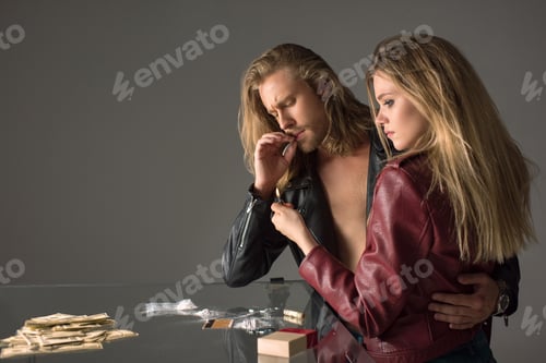 Preview: young addicted couple smoking cigarette with cocaine spilled on table on grey