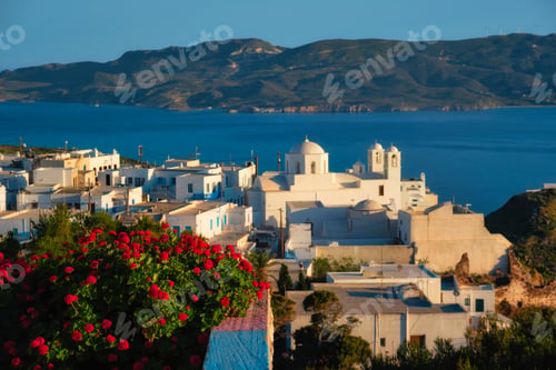 Preview: View of Plaka village on Milos island over red geranium flowers on sunset in Greece