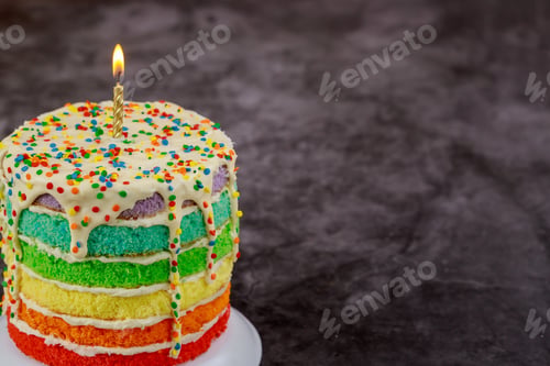 Preview: Birthday colorful rainbow layer cake with sprinkles and candle.