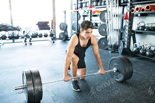 Preview: Young fit hispanic man in gym lifting heavy barbell
