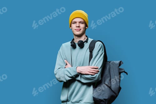 Preview: Young male in yellow cap sweatshirt with headphones backpack on blue background
