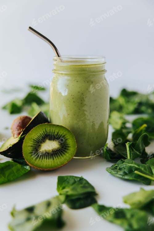 Preview: Closeup shot of a healthy fresh green shake, a half kiwi,a half avocado, and fresh spinach leaves