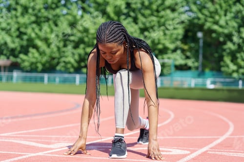 Preview: African American woman with long braids prepares low start running action on red track at stadium