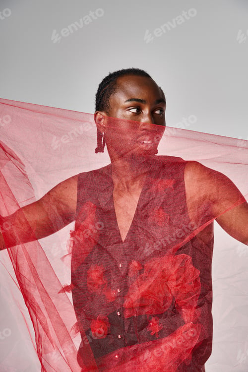 Preview: good looking young african american male model posing with vibrant red tulle fabric on gray backdrop