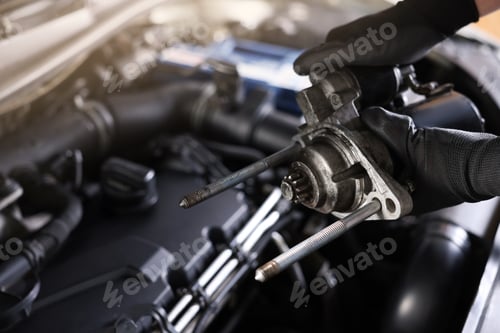 Preview: Auto part. Professional mechanic with starter motor near open hood of car indoors, closeup