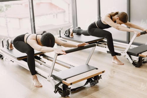 Preview: Two girls in a bright gym doing duet stretching with equipment