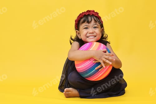 Preview: Smiling little girl sitting and holding colorful ball