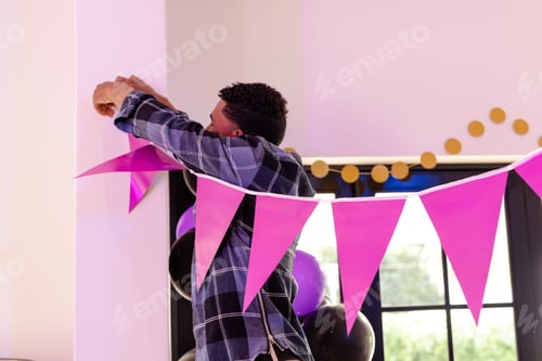 Preview: African American man decorating room with pink bunting for celebration event