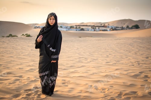 Preview: Arabic woman in traditional clothes standing in the desert in front of Bedouin village.