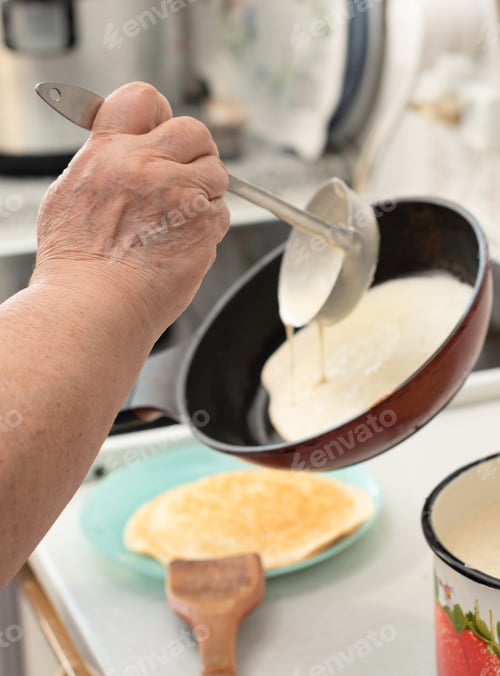 Preview: Senior woman chef pour portion of liquid dough by hands with ladle on frying pan for baking crepes