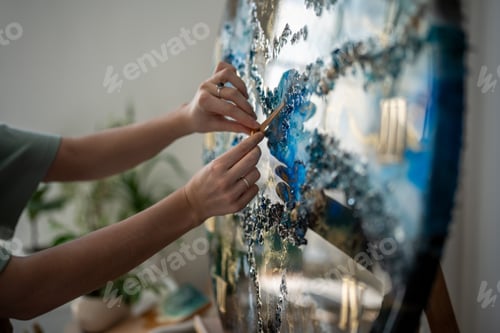 Preview: Graceful careful arms of female artist completing work on epoxy resin project, watch, clock.