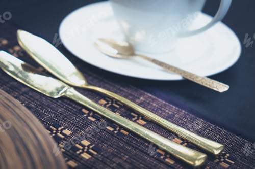 Preview: Detail of golden cutlery and a cup laid on a table