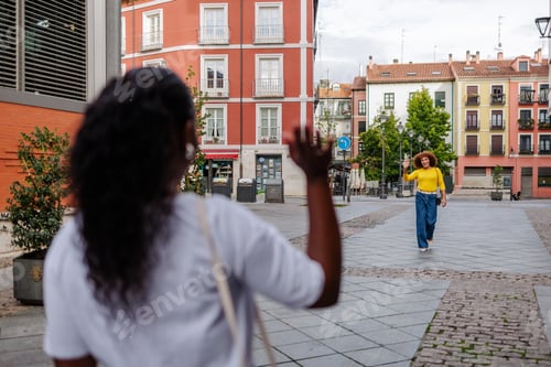 Preview: Rear view of black woman greeting and gathering her trans friend in city street. Friends meeting.