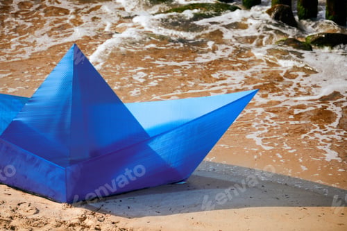 Preview: Origami blue paper boat on sandy beach for concept design, beautiful paper ship on shore, close up