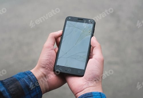 Preview: Closeup shot of a person's hand holding a cracked smartphone against a rusty wall background