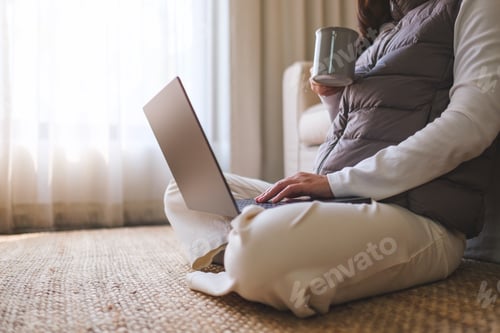 Preview: Closeup image of a woman drinking coffee while working on laptop computer at home