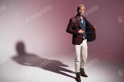 Preview: Young african man in red jacket standing on pink background