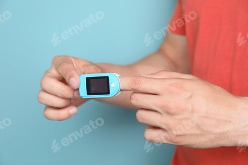 Preview: Young man checking pulse with blood pressure monitor on finger against color background, closeup