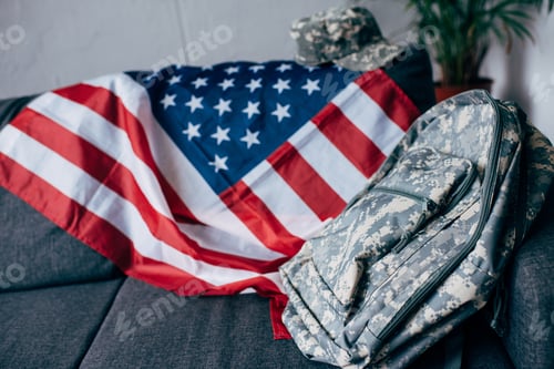 Preview: american flag, camouflage backpack and capat on sofa at home