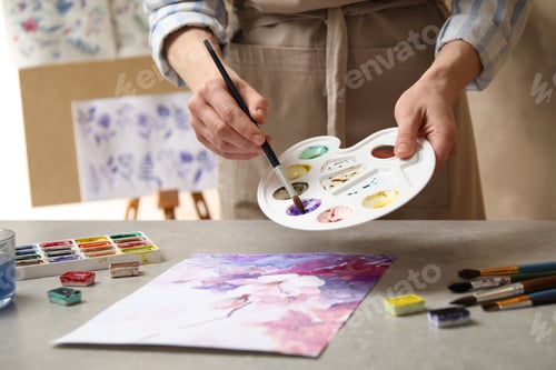 Preview: Woman painting flowers with watercolor at grey stone table in workshop, closeup