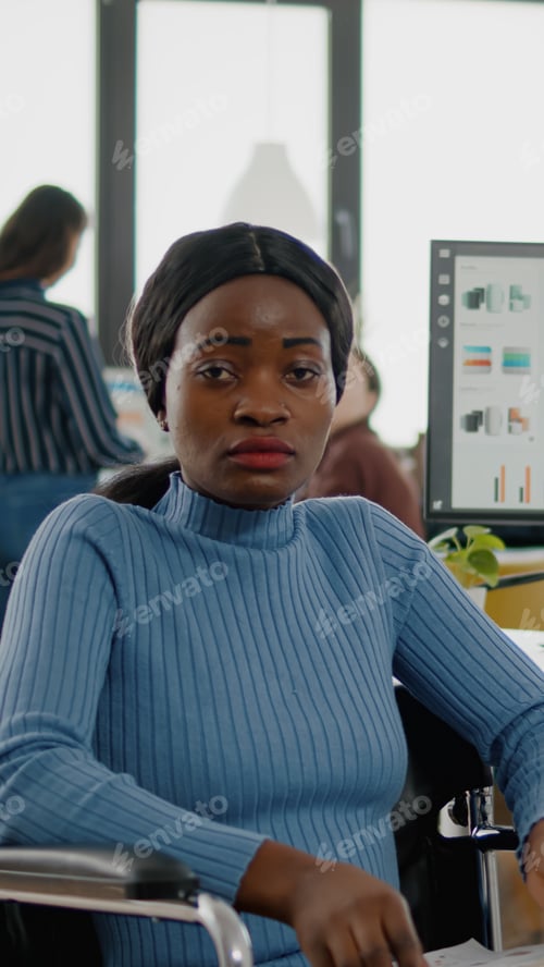 Preview: Black woman with disabilities looking at camera sitting in business office