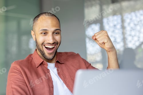 Preview: Cheerful man celebrating success while working on a laptop in an office