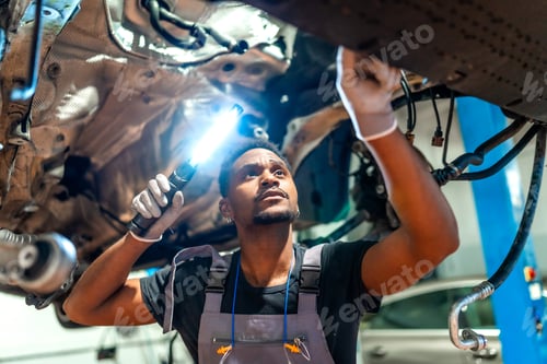 Preview: Mechanic inspecting car chassis with flashlight in auto repair shop