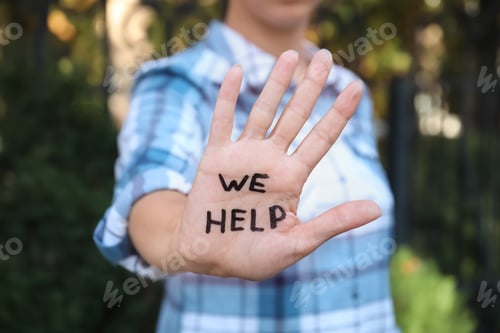 Preview: Woman showing hand with words "WE HELP" outdoors, closeup
