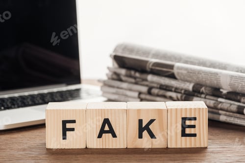 Preview: wooden cubes with word fake, laptop and newspapers on wooden tabletop