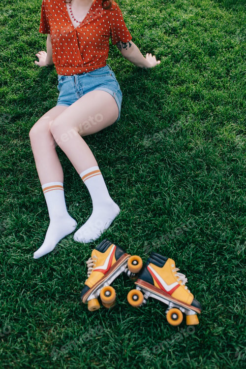 Preview: cropped shot of girl in denim shorts and socks resting on grass with roller skates
