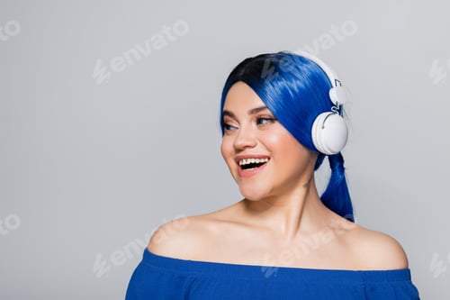 Preview: cheerful young woman with blue hair listening music in wireless headphones