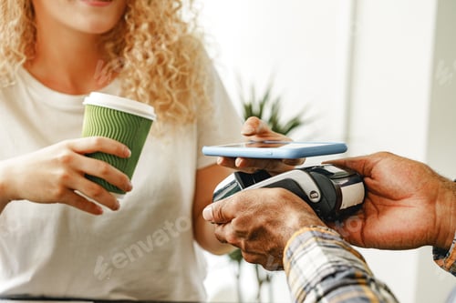 Preview: Woman customer of coffee shop paying for coffee through mobile phone using contactless technology