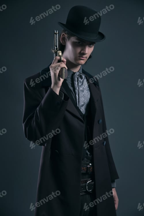 Preview: Western 1900 Fashion Man With Brown Hair And Hat Holding Gun. Studio Shot Against Grey.