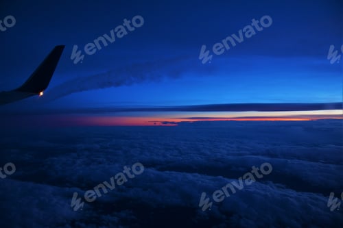 Preview: Beautiful shot of an airplane flying above white clouds at sunset