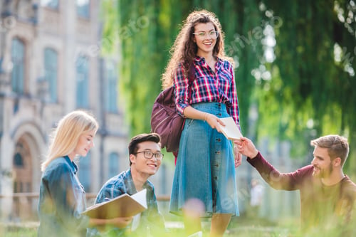 Preview: multiracial students studying in park with university on background