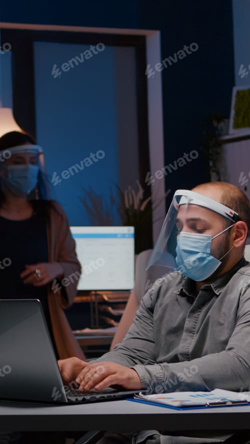 Preview: Workaholic businessman with face mask and visor against covid19 working in company office