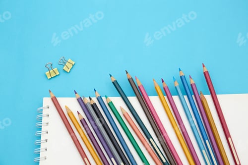 Preview: Top view of many colorful pencils and paper clips on a blank notebook