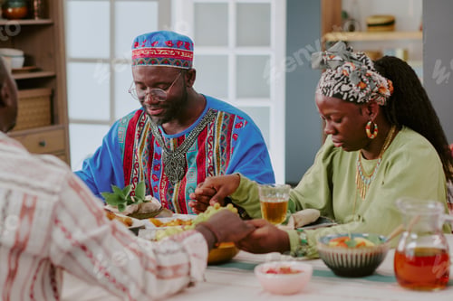 Preview: Black Family Celebrating Kwanzaa by Holding Hands and Praying at Table