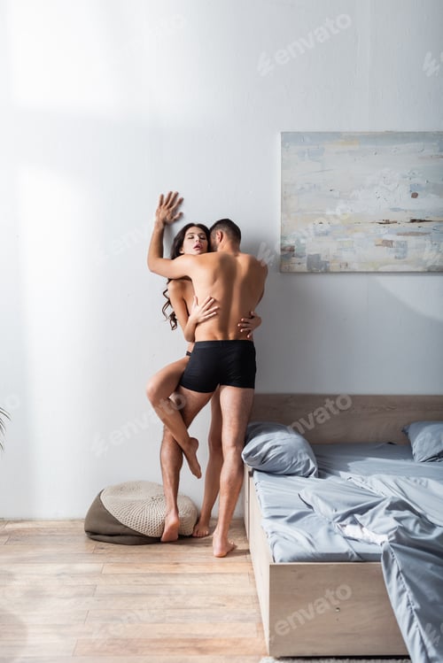 Preview: Muscular man in underpants kissing sexy girlfriend near bed at home